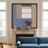 Cerulean Mist SQ130 textile wall art displayed above a fireplace mantel in a bright living room with a blue velvet sofa.