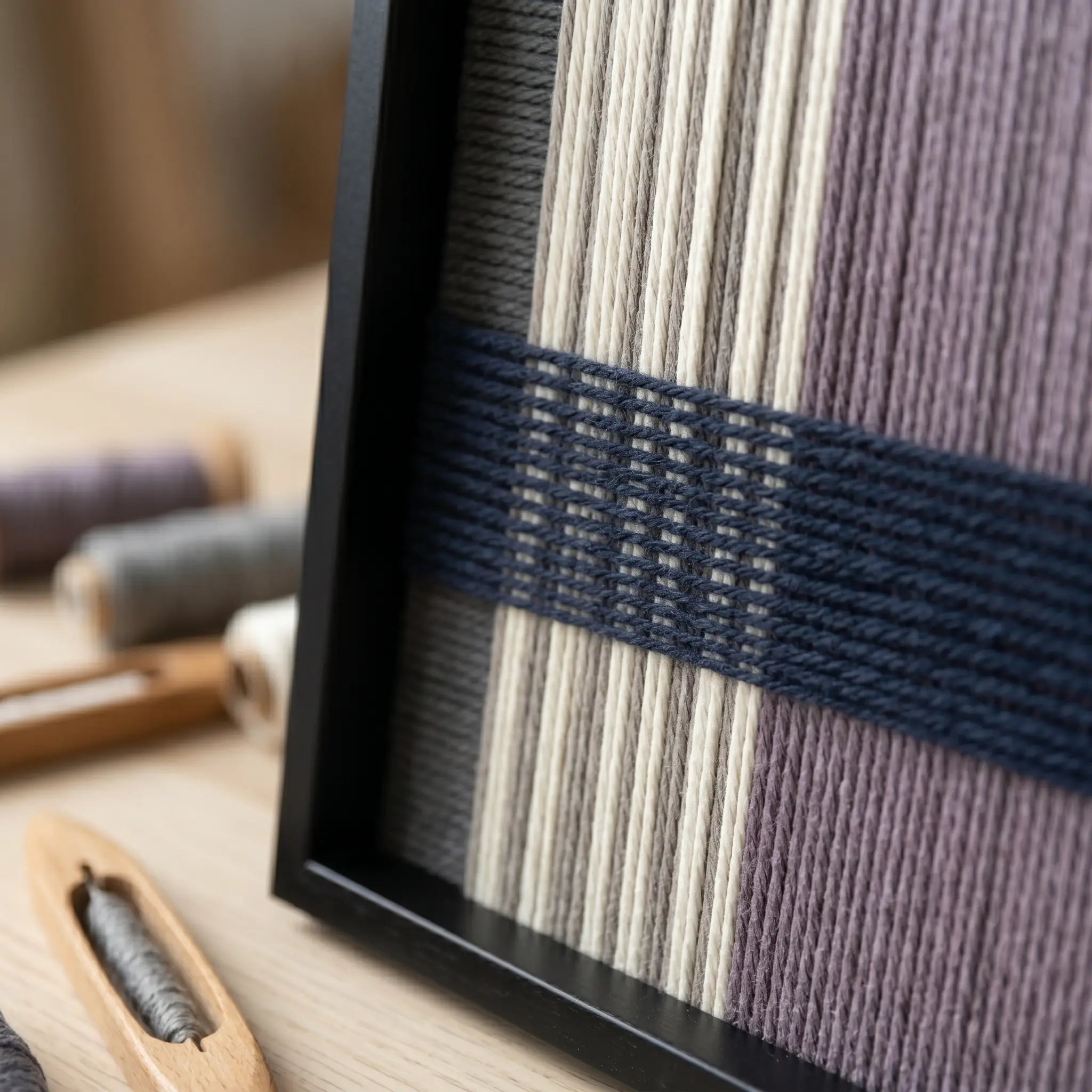 Angled close-up of Midnight Lavender SQ134 showing the black frame and dimensional navy lines over cream and lavender yarn.