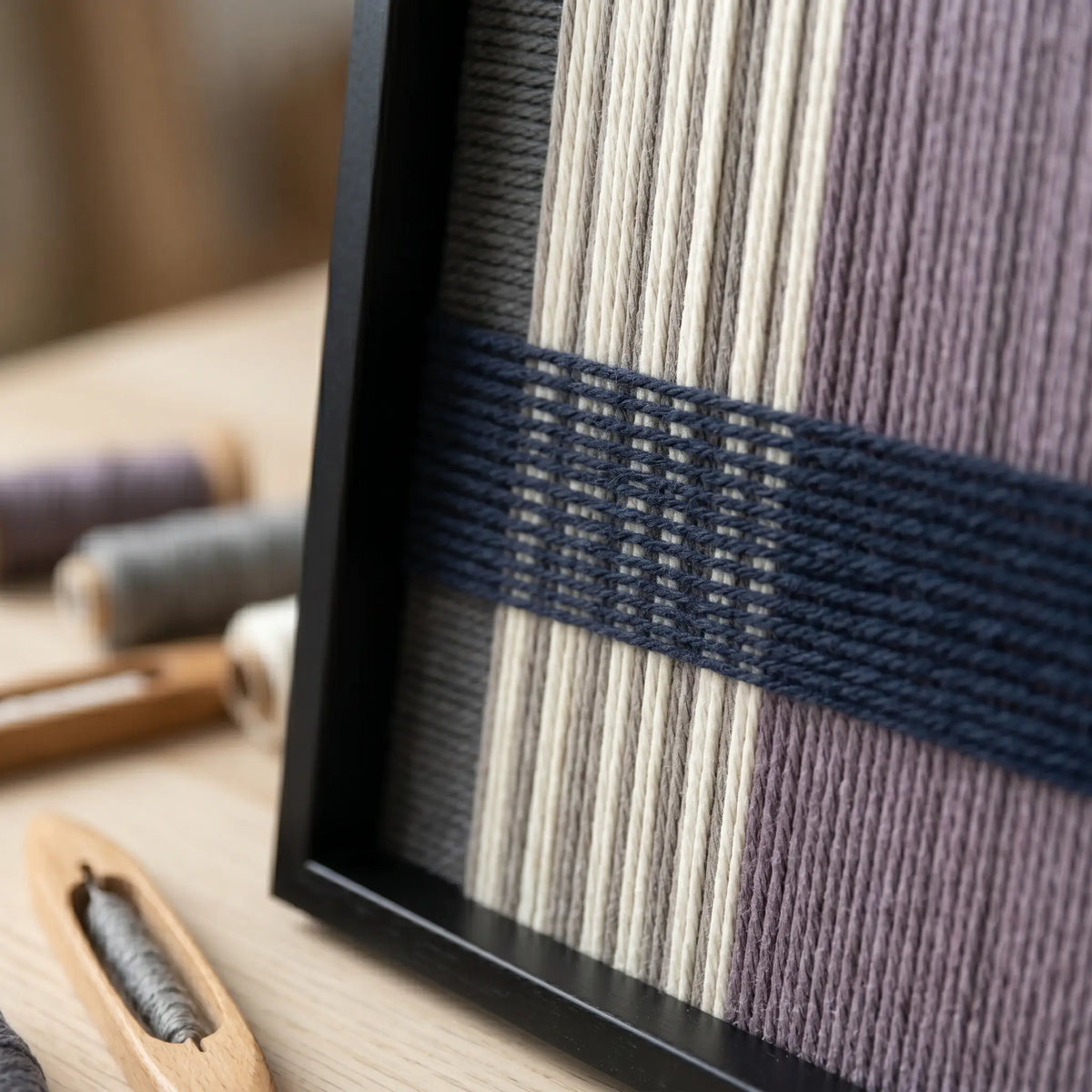 Angled close-up of Midnight Lavender SQ134 showing the black frame and dimensional navy lines over cream and lavender yarn.