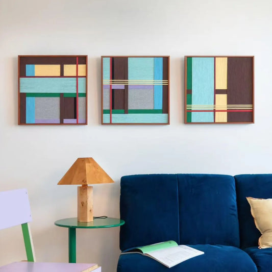 Three Rhythms of Silence SQ142 textile artworks displayed together above a blue sofa in a modern living room.