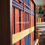 Detail of Constructed Mind framed textile wall art, featuring navy cotton cord with terracotta grid bands and a yellow vertical accent.