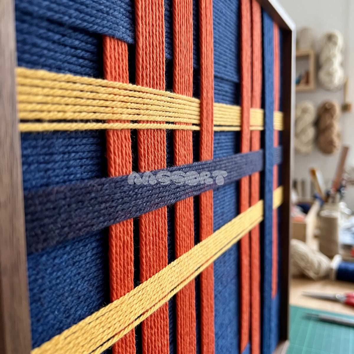 Detail of Silent Axis framed textile wall art, featuring navy, terracotta, and wheat yellow cotton cord arranged in an architectural grid.