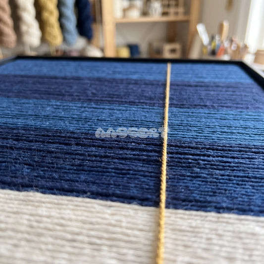 Blue Threshold textile art detail: low-angle view of the fine gold-colored strand crossing blue and cream fibers.