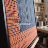 Held Space textile art detail: rust-orange horizontal strands meeting navy vertical fibers.