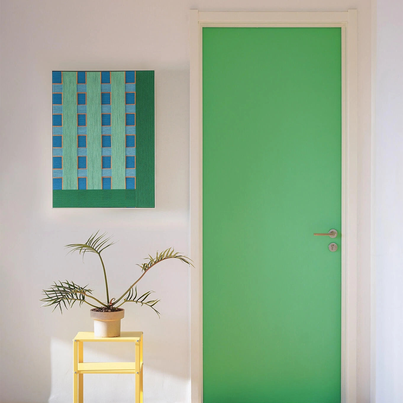 A smaller square version of the hand-woven wall decor hanging next to a bright green door, showcasing cohesive color matching in interior design.