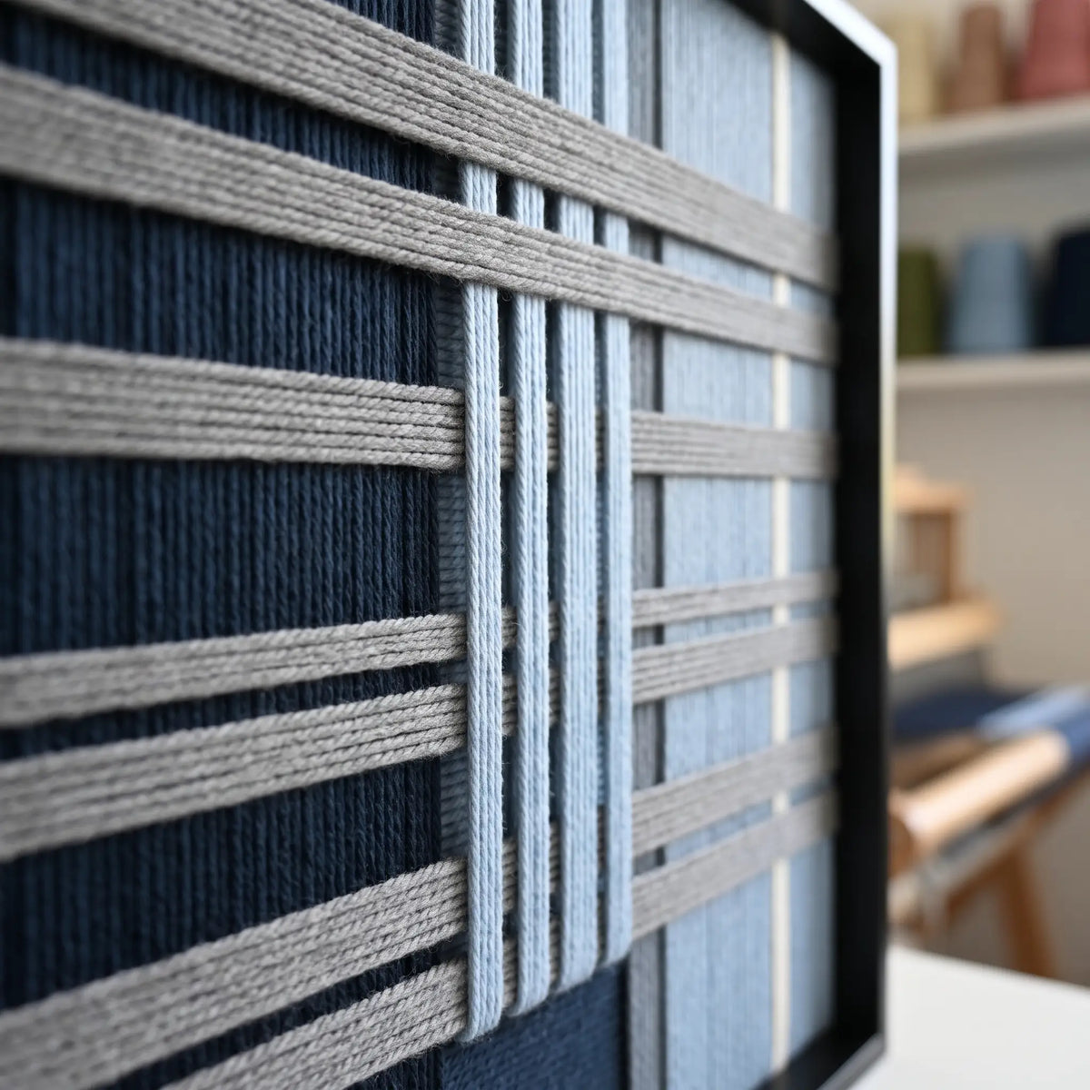 Angled close-up of the Starry Latitude framed wall art highlighting the dimensional navy and cream woven wool yarn patterns.
