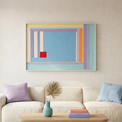 Large-scale textured fiber wall art centered above a cream couch with colorful accent pillows in a contemporary sunlit lounge.