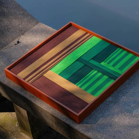 Hand-held view of Summer Mountain Walk yarn wall art showing its compact square form, precise stripe alignment, and sturdy wood frame.
