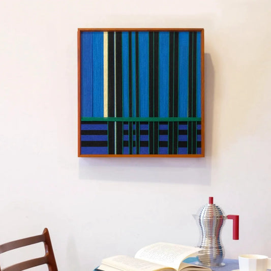 Summer Night’s Serenity hand-woven yarn wall art with alternating navy and forest green vertical stripes and a mint-green accent line, framed in natural wood and displayed on a console table
