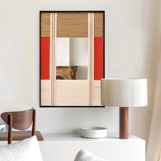 The Sun Always Rises hand-woven yarn mirror wall art with central reflective panel, oatmeal and natural wool stripe borders, and a bold red accent stripe, framed in black wood and displayed on a console table.
