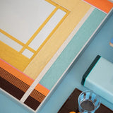 Angled tabletop detail of the Sun-Drenched Days yarn-framed mirror showing orange, yellow, aqua, cream, and brown wrapped-fiber sections.