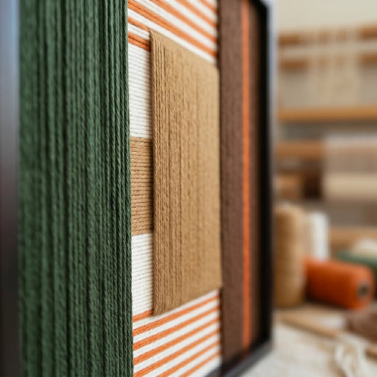 Macro shot of Sylvan Glow hand-woven wool art showing the deep forest green, terracotta, and ochre yarn textures in a black frame.