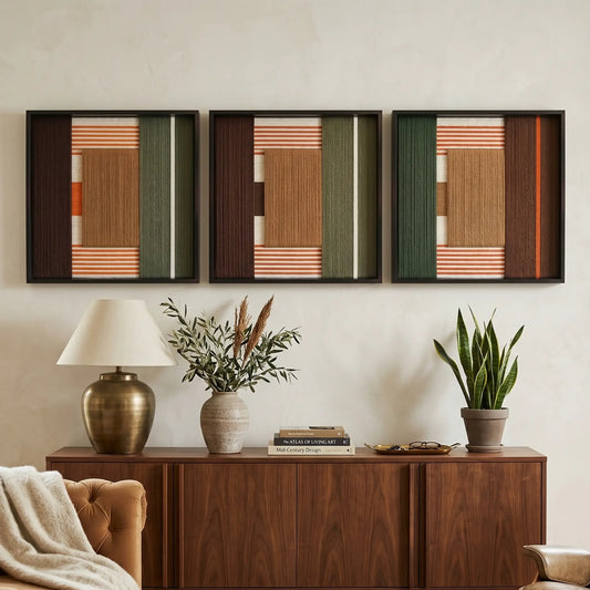 Triptych set of Sylvan Glow hand-woven textile artworks hanging elegantly above a dark wood mid-century sideboard styled with ceramics and a lamp.