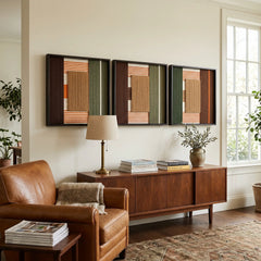 Sylvan Glow hand-woven textile art triptych styled above a dark wood sideboard next to a brown leather armchair in a sophisticated living space.