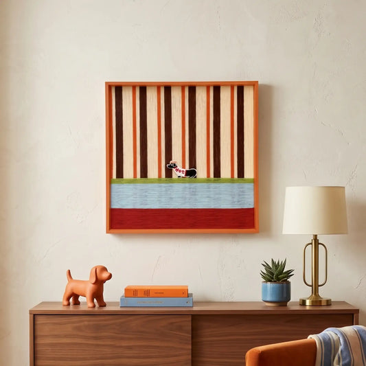 Hand-woven wool wall art in an orange frame featuring a dachshund motif on tangerine and brown stripes above a wooden credenza.