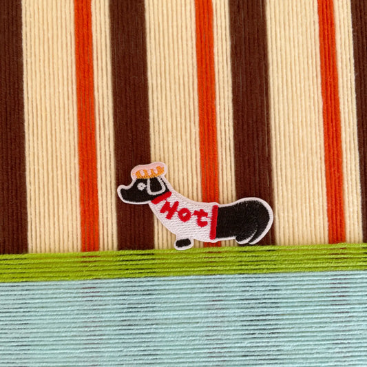 Close-up macro shot of the hand-woven wool texture and the whimsical dog character detail on the striped tapestry background.