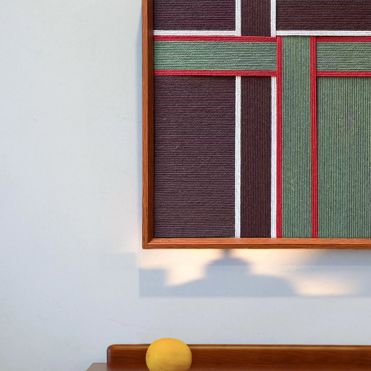 Angled shot capturing the depth of the wooden frame and the tactile surface of the textured red and green soft cotton cord fibers.