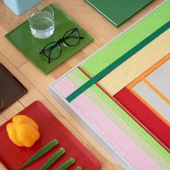 Close-up angled view of the hand-woven mirror frame on a desk, highlighting the vibrant green and pink wool texture against office accessories.
