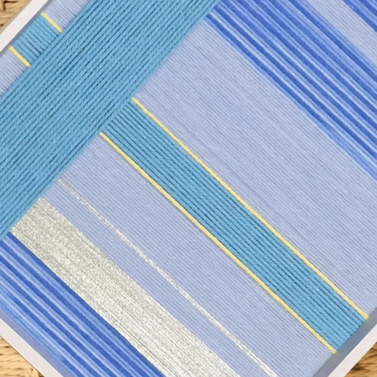 Flat lay of That Summer, the Blue Sea yarn wall art revealing its precise square form and uniform blue stripe weave
