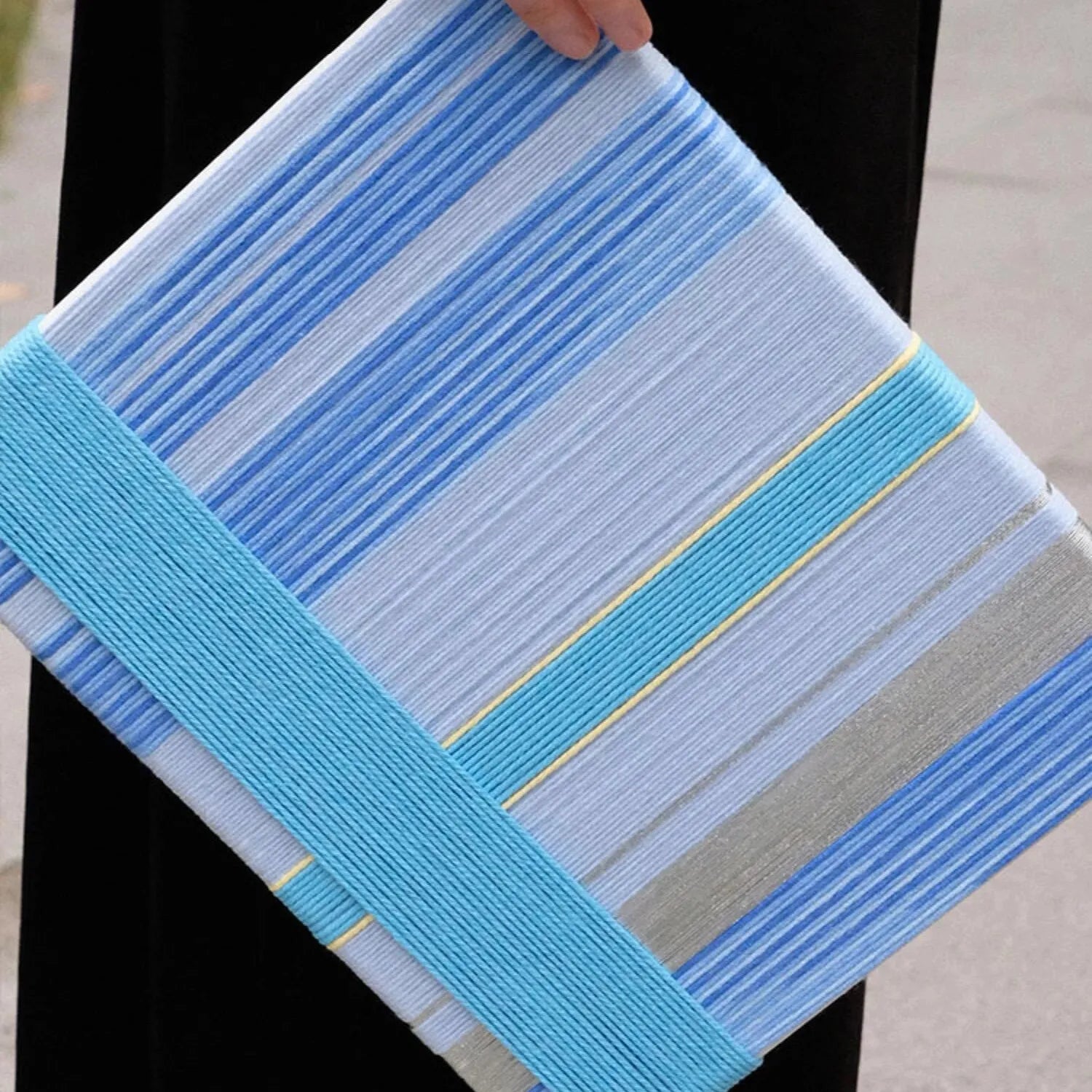 Hand-held view of That Summer, the Blue Sea yarn wall art showing its robust wood frame and compact square design
