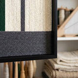 Close-up craftsmanship detail of The Interval textile wall art showing tightly wrapped forest green, cream, and charcoal yarn within a black frame.