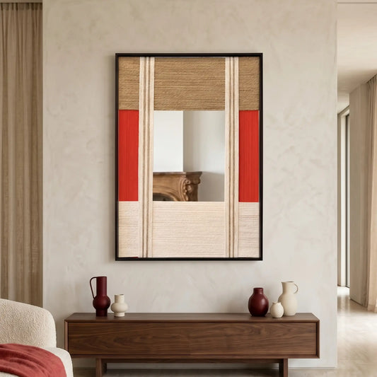 Vertical hand-woven wool wall art in a black frame with a central mirror inlay, featuring geometric panels in red, tan, and cream, hanging above a walnut sideboard with decorative vases.