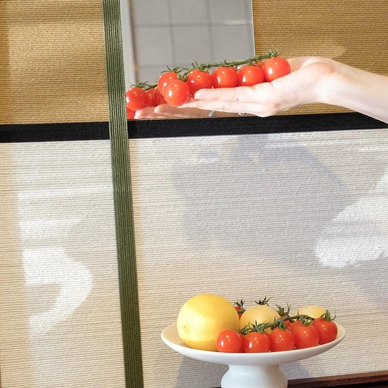 Close-up styling detail of the Through the Mirror yarn-framed mirror with red tomatoes and yellow fruit reflected in the glass.