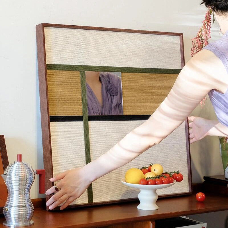 Hand‑held serving view of Through the Mirror mirror wall art as someone places fruit on the table, highlighting its reflective center and warm wool stripe borders.
