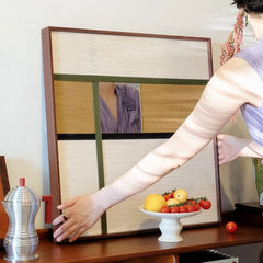 Hand‑held serving view of Through the Mirror mirror wall art as someone places fruit on the table, highlighting its reflective center and warm wool stripe borders.
