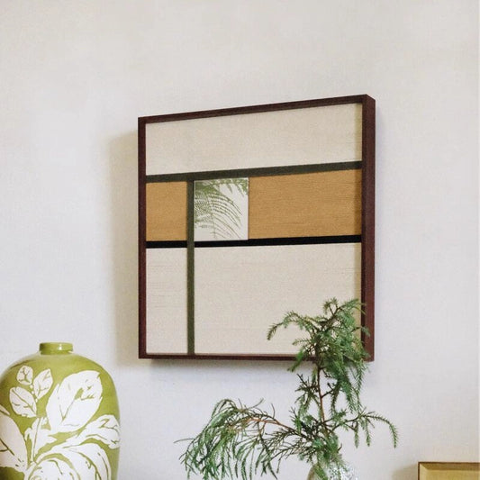 Through the Mirror yarn mirror art mounted on a wall beside potted greenery, showcasing its compact square form and harmonious stripe-and-mirror combination.
