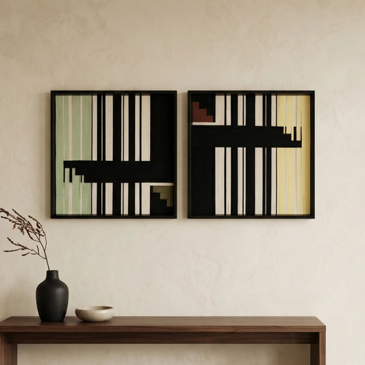 A diptych set of square hand-woven wool wall art in black frames, featuring minimalist black and cream geometric abstract patterns with sage green accents, hanging above a dark wood console.
