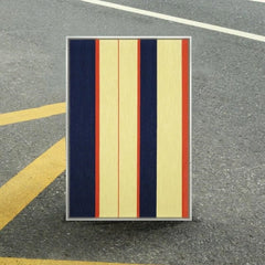 Twilight Rush hand-woven wool yarn wall art with alternating navy and cream vertical stripes accented by a slender coral stripe, framed in natural wood and displayed on an asphalt pavement.
