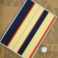 Twilight Rush yarn wall art resting on a tabletop beside a ceramic jar, highlighting its balanced stripe composition and tactile weave.
