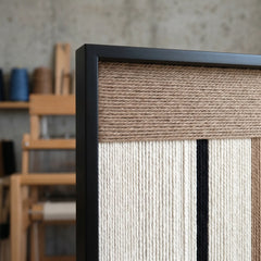 Detailed view of the hand-woven wool craftsmanship within the black frame, captured in a bright artist studio environment.