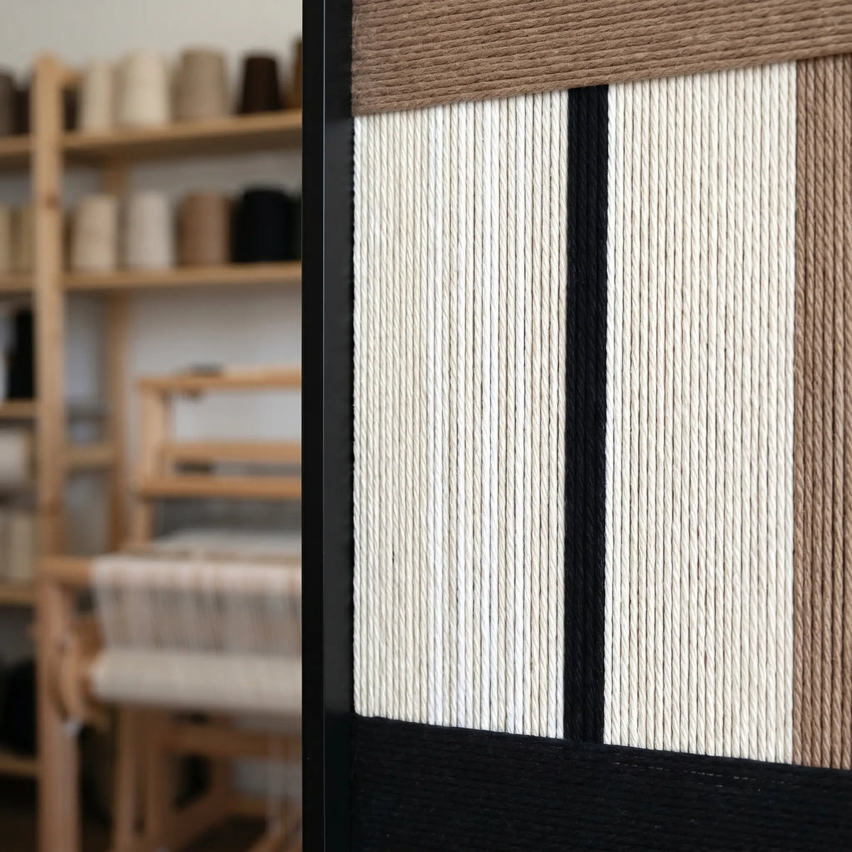 Side profile of the framed fiber art in a workshop setting, showcasing the depth and three-dimensional quality of the soft cotton cord threads.