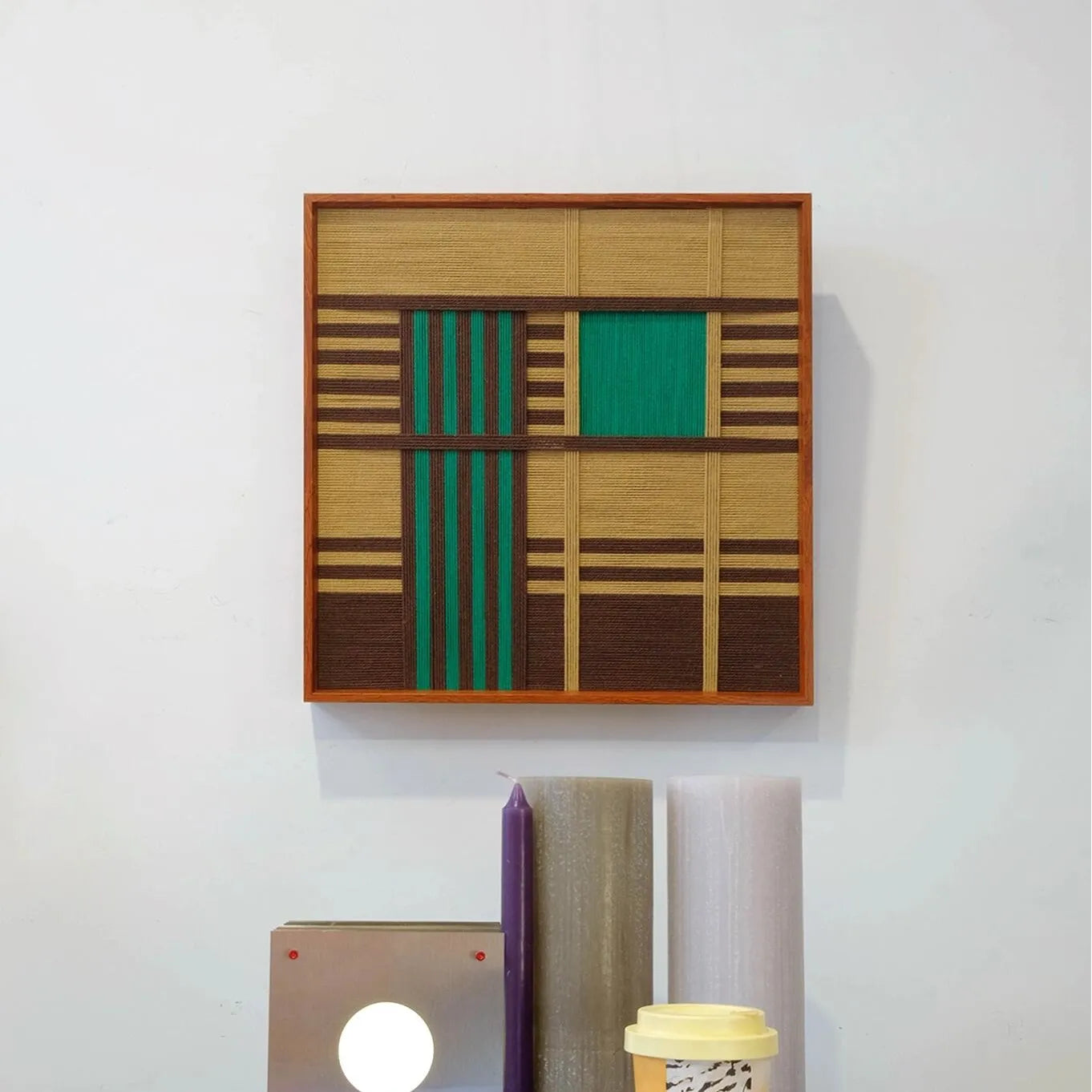 Vast Horizon yarn wall art positioned next to a laptop and notebook, emphasizing its square format and color-block stripe pattern
