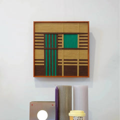 Vast Horizon yarn wall art positioned next to a laptop and notebook, emphasizing its square format and color-block stripe pattern
