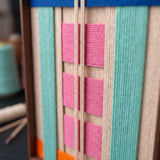 A detailed macro close-up of the Vegas Strip hand-woven wool tapestry featuring rich pink, teal, and orange geometric fibers.