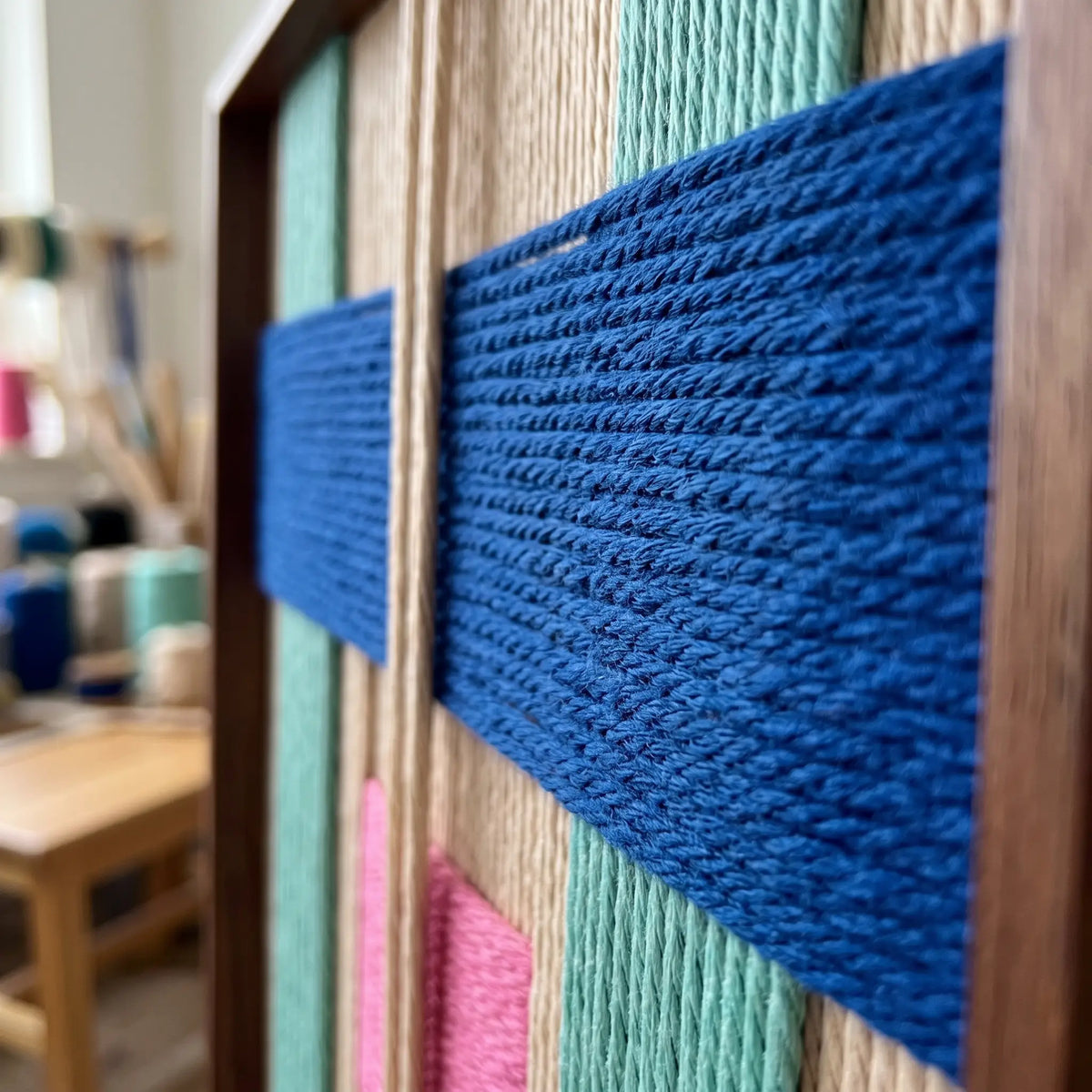 An angled side view of the Vegas Strip hand-woven wool tapestry highlighting vibrant blue, pink, and orange yarn textures.