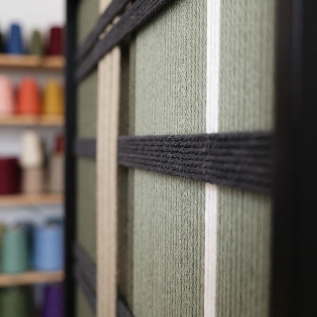 Extreme macro close-up of the Verdant Silence hand-woven wool tapestry showing textured green and black geometric yarn details.