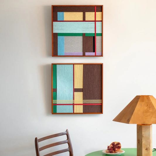 Two textured fiber art frames hanging vertically on a white wall, showcasing the geometric color block design in a minimalist interior.