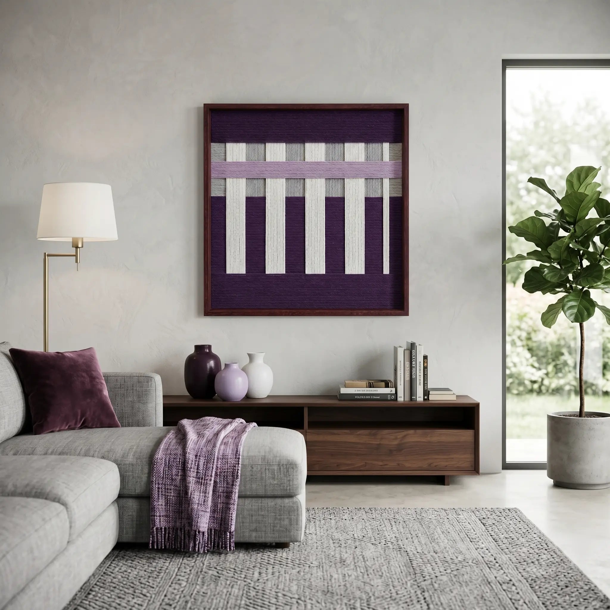 Textured wool wall decor in a dark frame placed above a wooden credenza in a bright, contemporary lounge with a grey sectional.