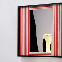 Wave Tide yarn mirror art resting on a tabletop beside a vase, emphasizing its precise stripe alignment and integrated reflective surface.
