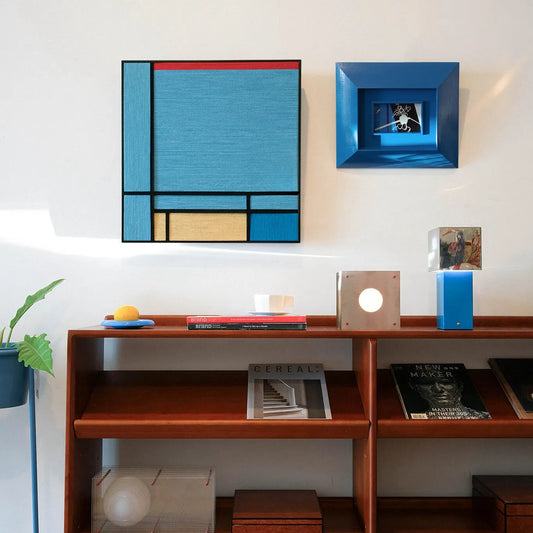 Angled view of Weave Reshape yarn wall art leaning against a tabletop, emphasizing tight wool weave and crisp transitions between sky-blue, mustard, red, and black panels.
