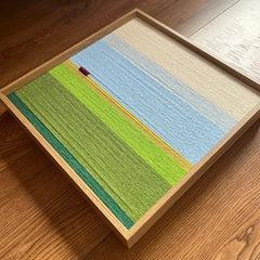 Angled overhead view of the hand-woven wool tapestry highlighting its horizontal yarn textures and landscape color blocking.