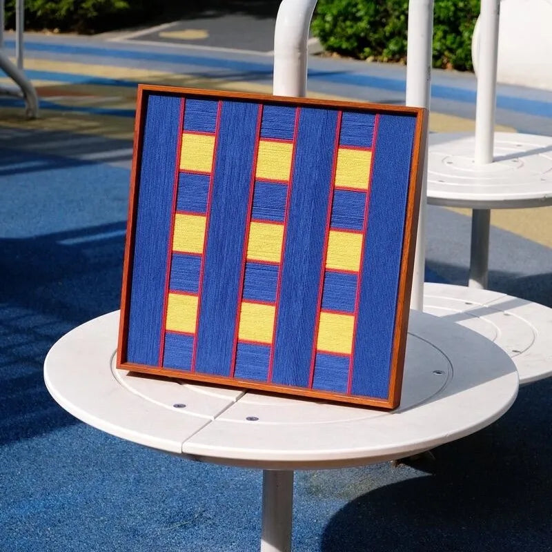 Window Peek at Moon square wall art displayed on a round side table outdoors with ceramic cup, highlighting its vivid blue geometric pattern
