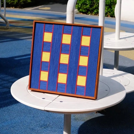 Window Peek at Moon square wall art displayed on a round side table outdoors with ceramic cup, highlighting its vivid blue geometric pattern
