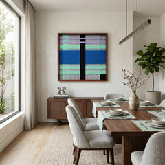 Large square Winter Aurora fiber wall art featuring cobalt blue, mint green, and black hand-woven patterns hanging in a modern dining room with a wood table.