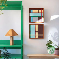 Hand-woven wool tapestry frames displayed on a green shelving unit, highlighting the vibrant interplay of brown, blue, and teal fibers.
